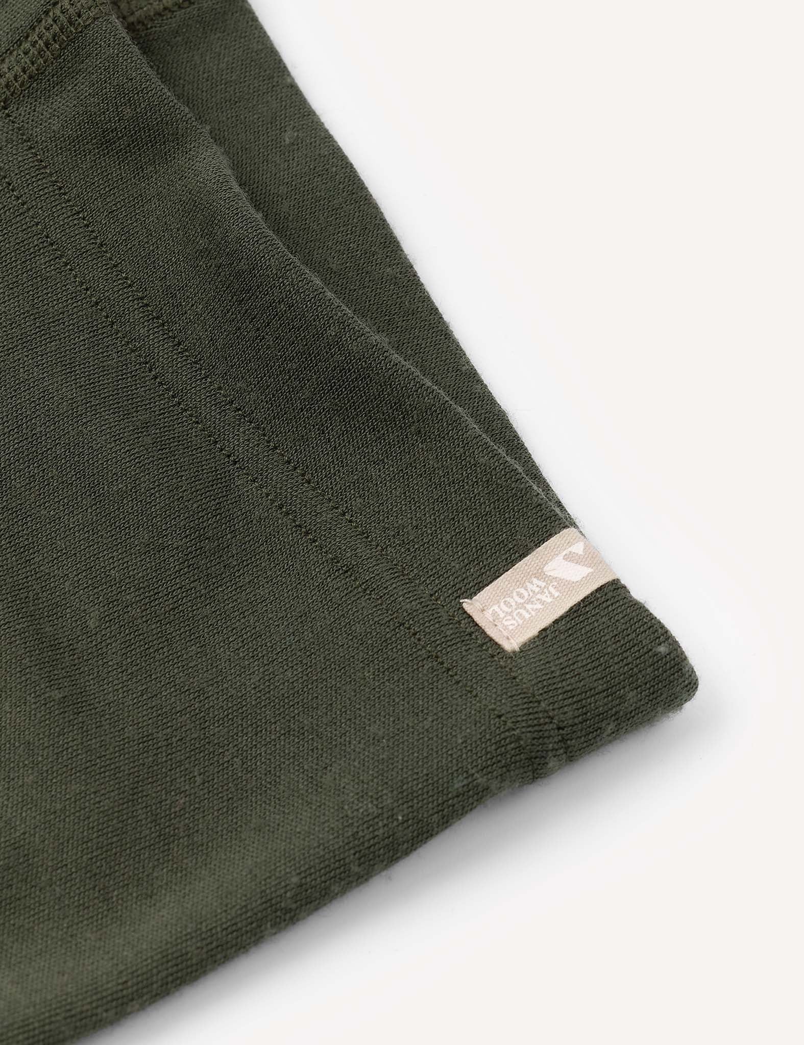 A close-up of a dark green fabric with a visible seam and a small beige tag that reads Global Organic Textile Standard, highlighting the warm and soft texture typical of the Merino Kids AirWool Leggings.