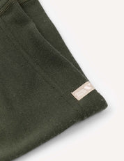 A close-up of a dark green fabric with a visible seam and a small beige tag that reads Global Organic Textile Standard, highlighting the warm and soft texture typical of the Merino Kids AirWool Leggings.