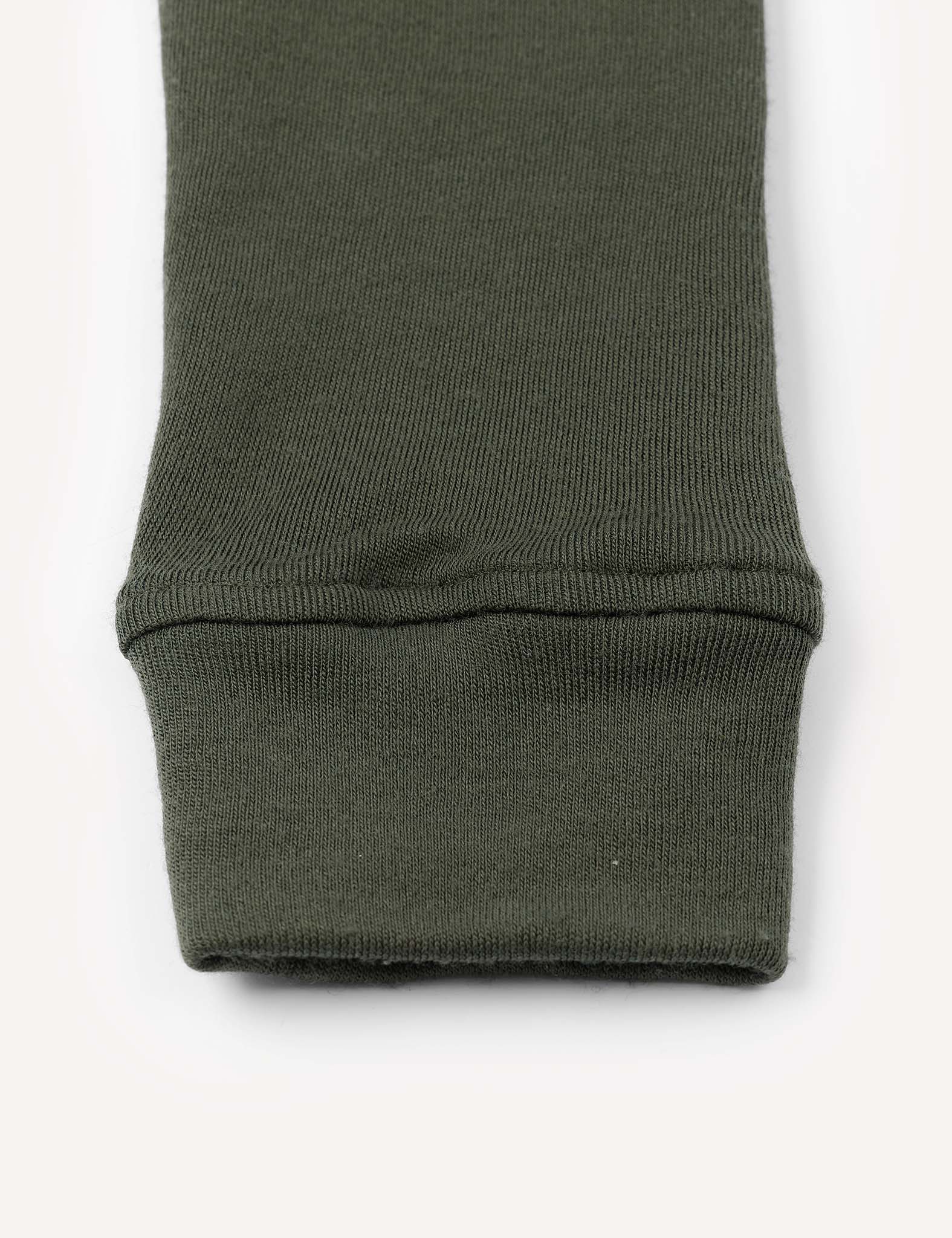 Close-up of the cuff of an olive green knit sleeve, laid flat on a light background. The fabric appears warm and soft, with a slightly ribbed texture at the cuff, characteristic of Leggings – Merino Kids AirWool.