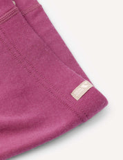 Close-up of the Merino Kids AirWool Leggings in magenta brushed wool, featuring visible stitching and a small beige tag. The soft fabric is displayed against a light, neutral background.