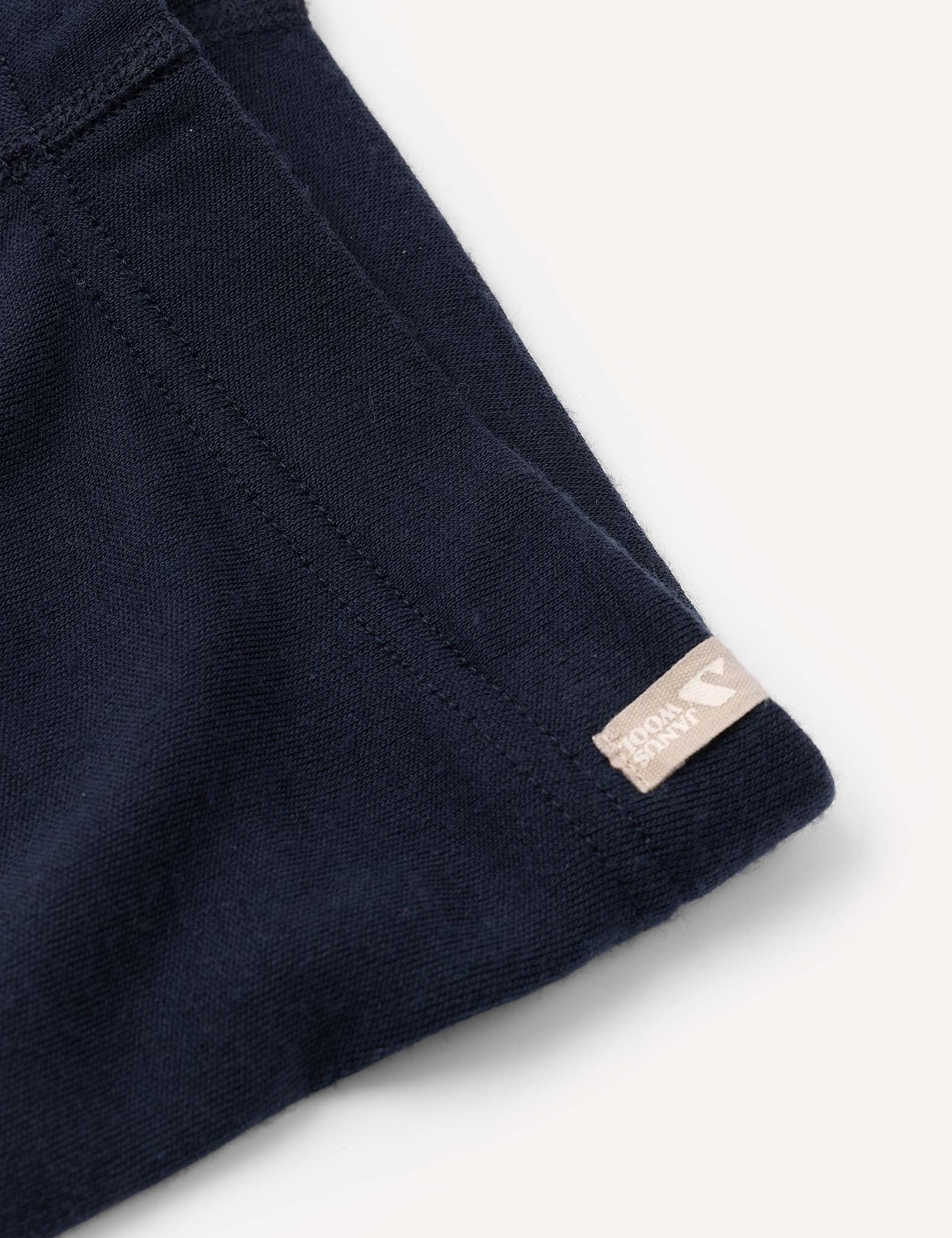 Close-up of the Leggings – Merino Kids AirWool in navy blue, featuring visible stitching and a small beige tag next to a small logo, highlighting the garment’s warm and comfortable brushed texture.