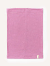 A mauve orchid, rectangular Neckwarmer – Merino Kids Light is laid flat on a white background, featuring visible stitching along the top and bottom edges and a small white tag sewn near one corner.