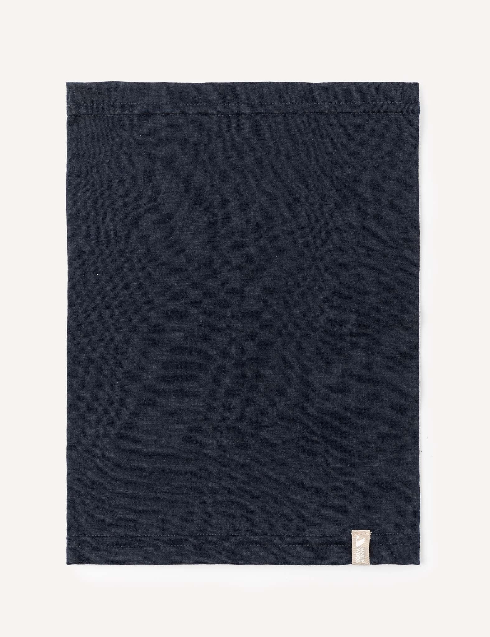 A neatly folded square piece of navy Neckwarmer – Merino Kids Light, featuring a small beige tag in the bottom right corner, placed on a light background.
