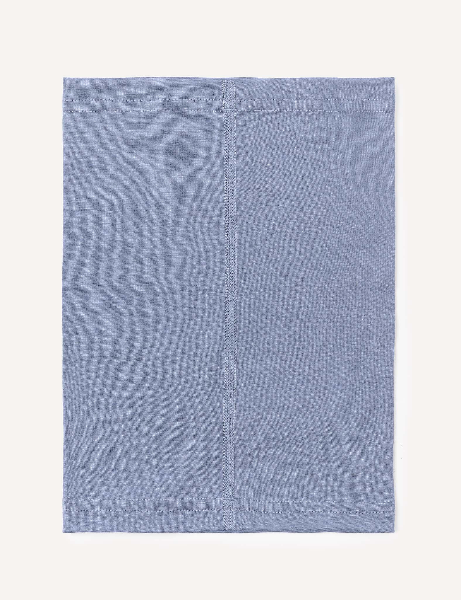 A light blue, square-shaped Neckwarmer – Merino Kids Light, featuring visible vertical and edge stitching, is displayed against a plain off-white background; it’s crafted from merino wool for excellent moisture transport.