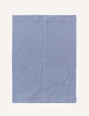 A light blue, square-shaped Neckwarmer – Merino Kids Light, featuring visible vertical and edge stitching, is displayed against a plain off-white background; it’s crafted from merino wool for excellent moisture transport.