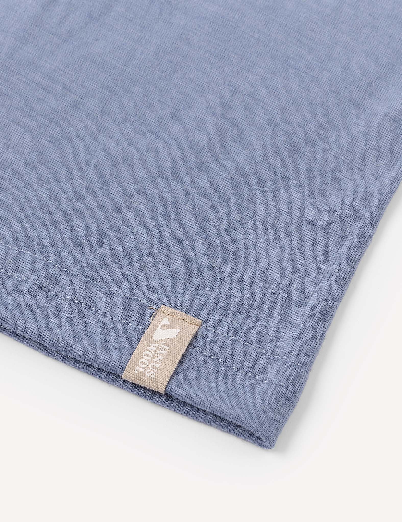 A close-up of the corner of a light blue Neckwarmer – Merino Kids Light, made from merino wool, with a beige tag.