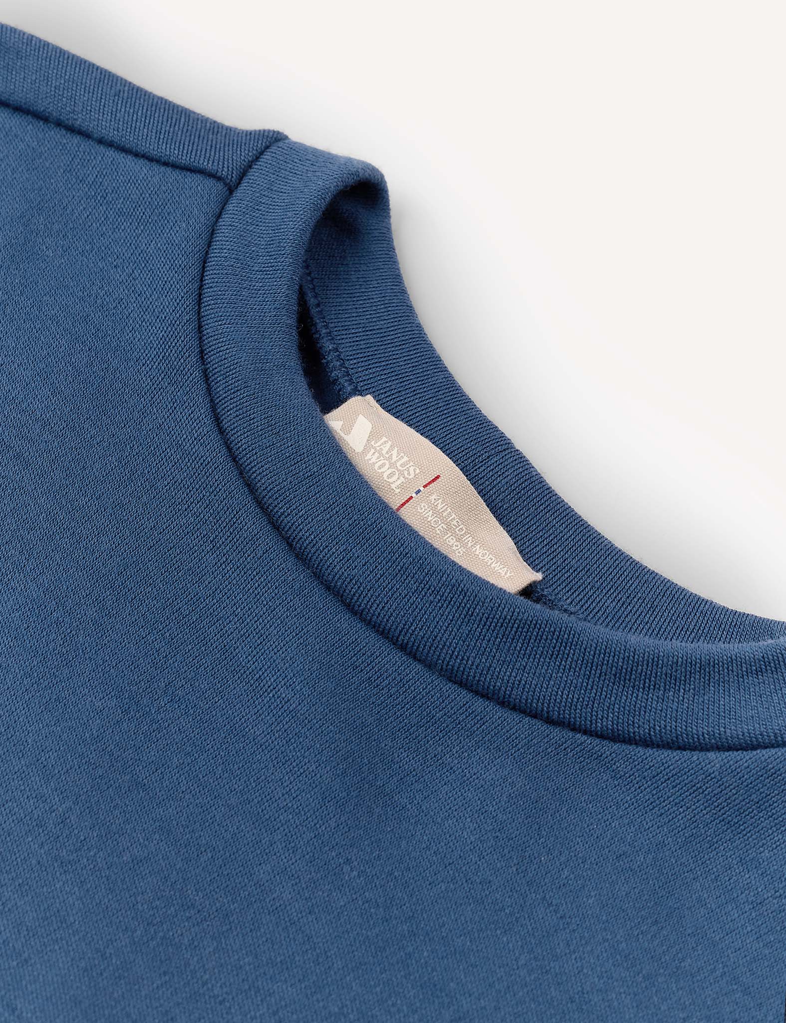 Close-up of the Pullover – Merino Kids AirWool in blue, highlighting the collar and a white inner label with red and gray text, set against a plain white background.
