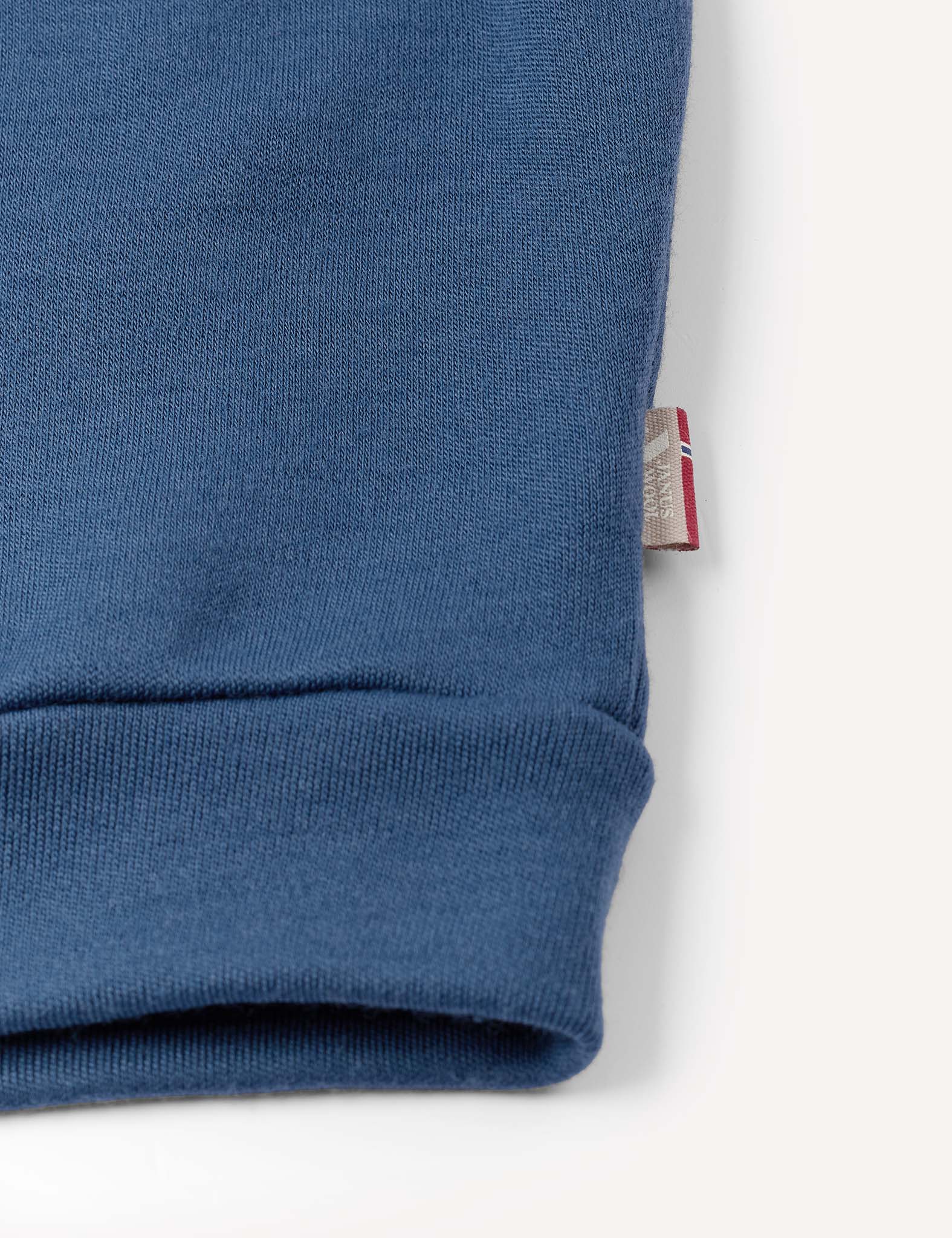A close-up of a blue Pullover – Merino Kids AirWool sweatshirt cuff on a white background, with a small fabric tag partially visible at the seam.