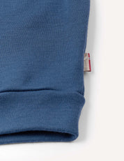 A close-up of a blue Pullover – Merino Kids AirWool sweatshirt cuff on a white background, with a small fabric tag partially visible at the seam.