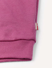 Close-up of the cuff of the Pullover – Merino Kids AirWool in pink, highlighting its visible knit texture and a small fabric tag with red and white stripes sewn into the side seam.