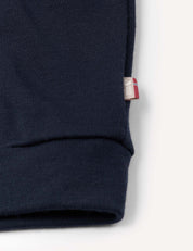 Close-up of the navy blue cuff of the Pullover – Merino Kids AirWool sweater, featuring a small fabric tag on the seam with red, white, and blue details.