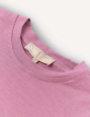 A close-up of the neckline and label of the T-Shirt – Merino Kids Light in mauve merino wool. Celebrated for its natural temperature-regulating properties and all-day comfort, the shirt is shown laid flat on a white surface.