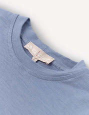 Close-up of a T-Shirt – Merino Kids Light in light blue, highlighting the collar and a beige tag featuring the brand name and care instructions. The detailed view of the merino wool fabric texture and precise stitching emphasizes its natural temperature-regulating properties for all-day comfort.