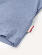 Close-up of the hem of the T-Shirt – Merino Kids Light in light blue, highlighting detailed stitching and a small fabric tag featuring red, white, and blue stripes on the right side. This merino wool garment is crafted for all-day comfort and natural temperature regulation.